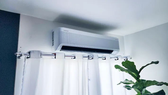 ar condicionado instalado numa parede branca com cortinas, o sol entra pela janela.